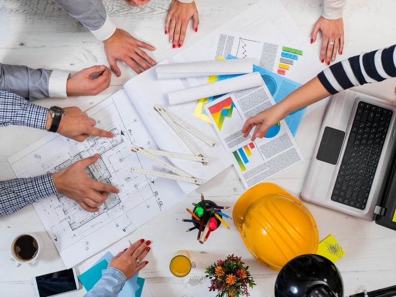 Construction project management team reviewing plans and schedules to coordinate multiple phases of a large development project.
